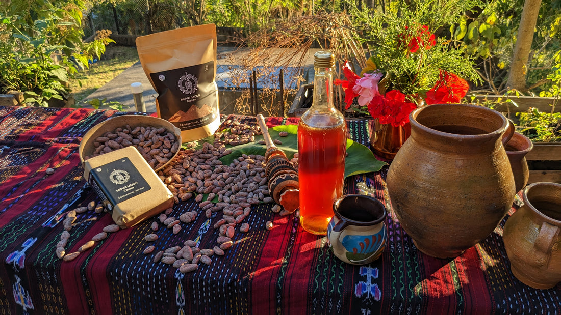 image of the elements for a cacao ceremony all set together on a mayan hand woven textile that lays in the grass on a morning vibe and vivid color,  the image includes spices and honey as sweetener.  